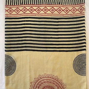 May include: Cream-colored fabric with a black and red geometric pattern. The design includes black stripes, vertical lines, and circular and diamond shapes. The fabric is likely used for textiles or home decor.