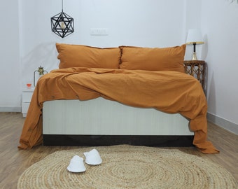 May include: A bedroom with a bed made with a brown duvet cover and two matching pillows. The bed is on a wooden floor with a jute rug in front of it. There are two white slippers on the rug.