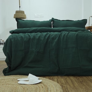 Può includere: Un copripiumino e federe in lino verde scuro su un letto con testiera bianca. La biancheria da letto è fatta con cura e il piumino è ripiegato per rivelare le lenzuola bianche sottostanti.