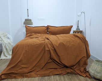 May include: A rust-coloured duvet cover with matching pillowcases. The duvet cover has a button closure at the bottom and is made of a soft, textured fabric.