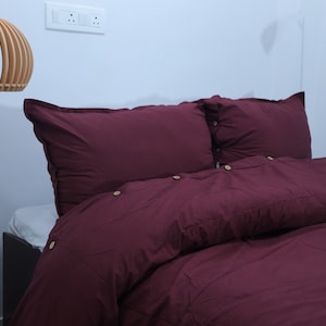 May include: A burgundy duvet cover with button closures and two matching pillowcases. The bedding is on a bed with a wooden headboard.