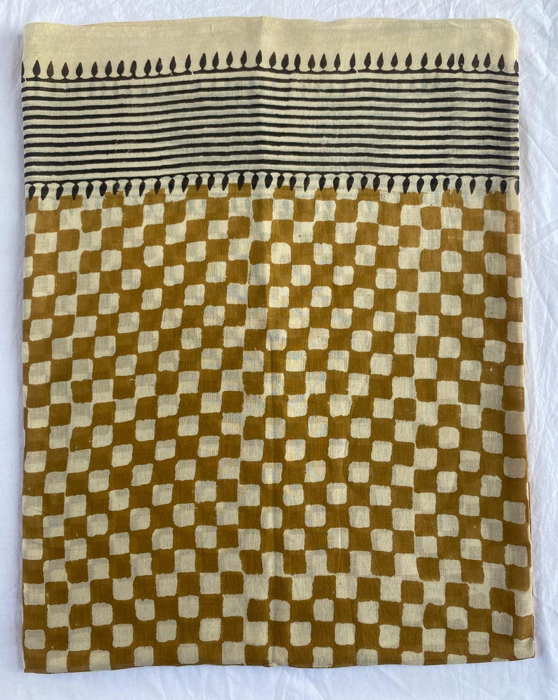 May include: A textile with a cream-colored top border featuring a black leaf-like pattern. Below are horizontal black stripes, followed by a mustard yellow and cream checkered pattern. The fabric is likely cotton or linen.