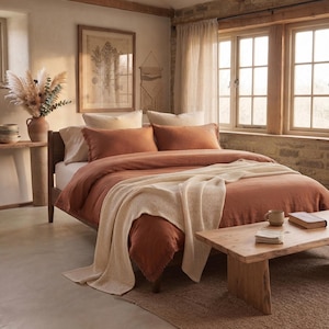 Pode incluir: Uma cama com capa de edredão cor de ferrugem e fronhas a condizer, coberta com uma manta de malha waffle cor de creme. A cama tem uma estrutura de madeira e está situada numa sala com um banco de madeira, um vaso de plantas secas e janelas.