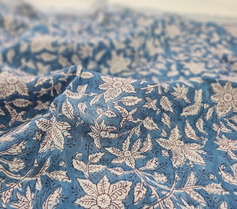 K&ouml;nnte beinhalten: Blauer Baumwollstoff mit einem wei&szlig;en und roten Blumendruck. Der Stoff ist weich und texturiert und eignet sich perfekt f&uuml;r Bastel- oder N&auml;hprojekte.