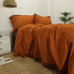 以下が含まれることがあります： オレンジ色のベッドセット。デュベカバー、枕カバー2つ、ベッドスカートが含まれています。白いナイトスタンド、花瓶、本、水が入ったグラスも写っています。ベッドルームのインテリア。