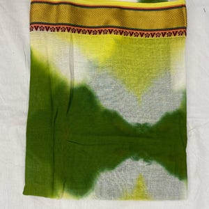 Op de afbeelding: Een witte, groene en gele tie-dye stof met een gouden en rode rand. De stof heeft een zachte, vloeiende textuur.