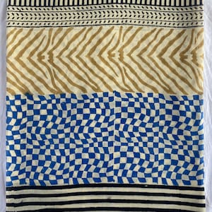 May include: A folded textile with a repeating pattern. The top and bottom borders feature black stripes. The middle sections display a tan zebra stripe design and a blue and white checkerboard pattern. The textile is likely made of cotton or linen.