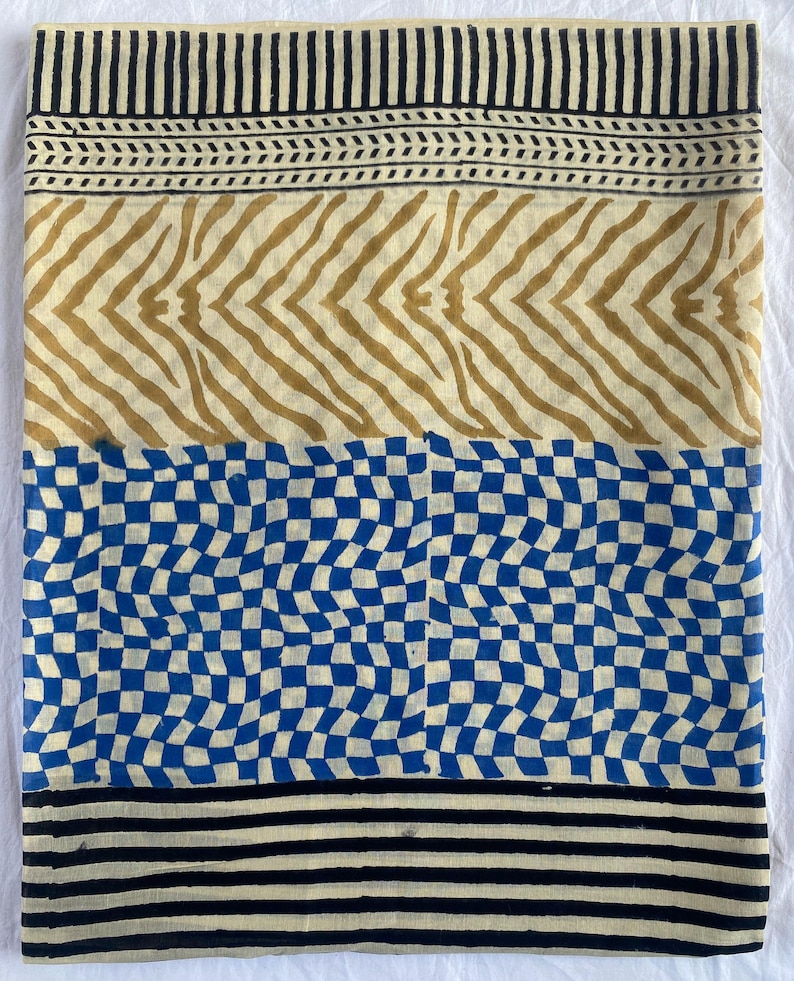 May include: A folded textile with a repeating pattern. The top and bottom borders feature black stripes. The middle sections display a tan zebra stripe design and a blue and white checkerboard pattern. The textile is likely made of cotton or linen.