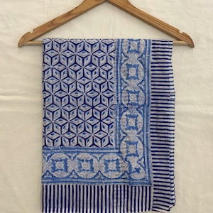 Op de afbeelding: Een blauwe en witte katoenen stof met een geometrisch patroon. De stof is gevouwen en hangt aan een houten hanger.