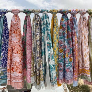 May include: A collection of 10 colorful cotton scarves with floral and geometric patterns. The scarves are hanging on a clothesline.