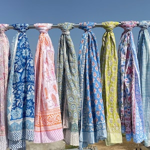 May include: Ten rectangular scarves hanging on a metal rod, each featuring distinct block-printed patterns in various colors including blue, green, pink, orange, yellow, and purple, with floral, fish, and geometric motifs on lightweight fabric.