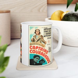 May include: White ceramic mug with a vintage movie poster design featuring the text "Captains Courageous" and the actors Freddie Bartholomew, Spencer Tracy, Lionel Barrymore, and Melvyn Douglas. The poster is in red, yellow, blue, and white.