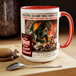 Peut inclure: Mug en céramique blanche avec intérieur et anse rouges. Le mug présente un design d'affiche de film vintage avec un monstre vert attaquant une ville. Le texte comprend "The Beast From 20,000 Fathoms".