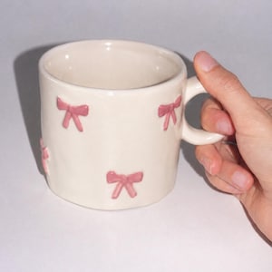 手描きのピンクのリボンが描かれたセラミックマグカップ、キュートなコーヒーカップ、彼女への可愛いギフト