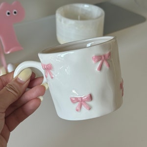 手描きのピンクのリボンが描かれたセラミックマグカップ、キュートなコーヒーカップ、彼女への可愛いギフト