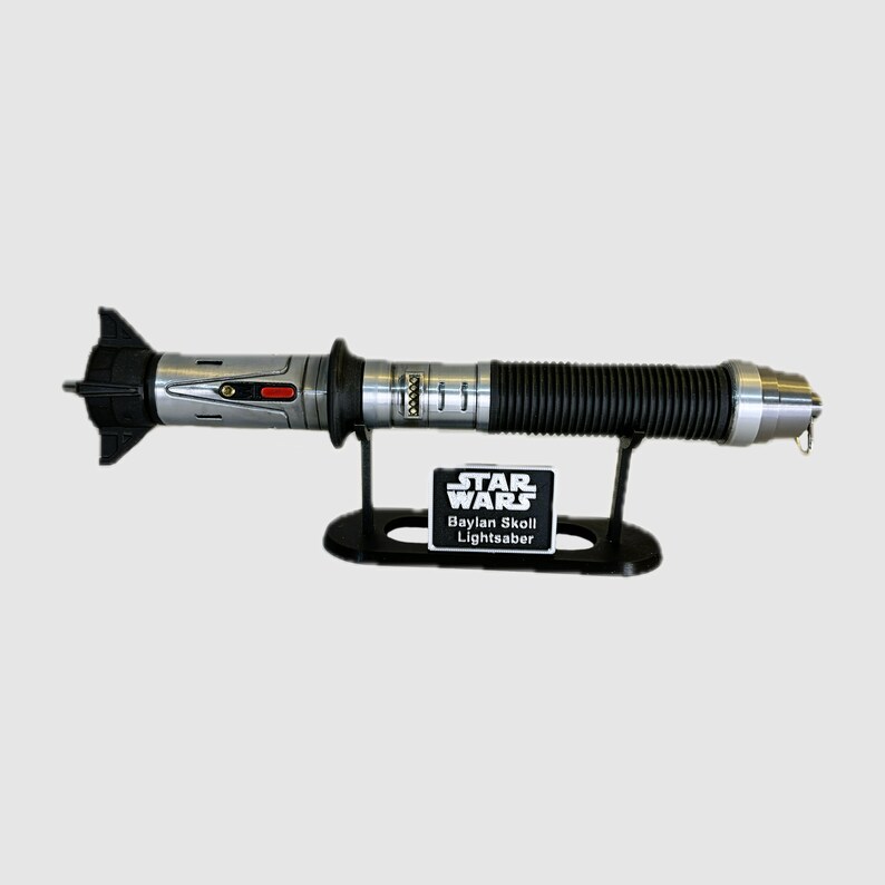 May include: A silver and black lightsaber with a black stand and a black label that reads "STAR WARS Baylan Skoll Lightsaber".