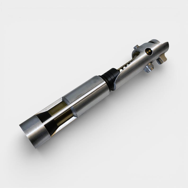 May include: A silver-colored lightsaber prop with a detailed design. The prop has a cylindrical body with a black grip and a partially exposed internal structure. The end features a series of metallic components and a small, circular button.