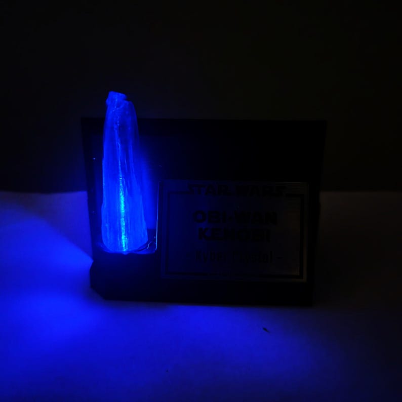 May include: A dark, rectangular object with a glowing blue crystal formation. The crystal is vertically oriented and emits a bright, ethereal light. A small, rectangular label is visible on the object.