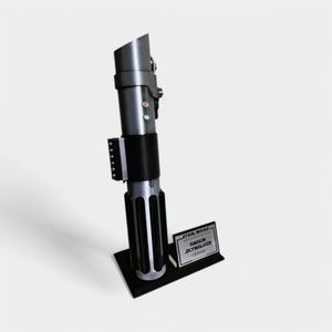 May include: A black lightsaber replica with a silver blade and a black stand. The stand has a silver plaque that reads "STAR WARS - EPISODE III - REVENGE OF THE SITH - ANAKIN SKYWALKER - Lightsaber"