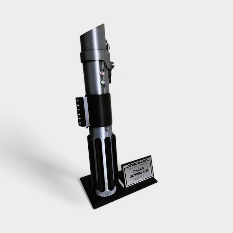 May include: A black lightsaber replica with a silver blade and a black stand. The stand has a silver plaque that reads "STAR WARS - EPISODE III - REVENGE OF THE SITH - ANAKIN SKYWALKER - Lightsaber"