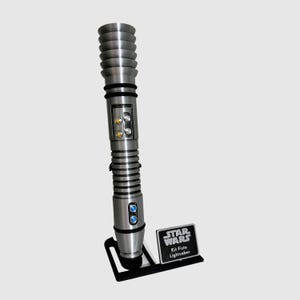 May include: A silver lightsaber with a black handle and a black stand. The stand has a silver plaque that reads "Star Wars" and "Kit Fisto Lightsaber".