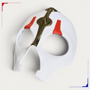 May include: A white full-face mask featuring a central metallic gold-toned crest that extends from the forehead to the nose area. The mask includes two large eye openings and is accented with symmetrical red markings above each eye socket.