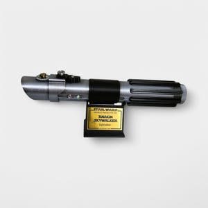May include: A silver and black lightsaber with a gold plaque that reads "STAR WARS Featuring the Adventures of the Jedi ANAKIN SKYWALKER - Lightsaber".