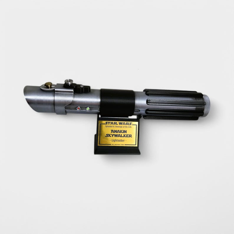 May include: A silver and black lightsaber with a gold plaque that reads "STAR WARS Featuring the Adventures of the Jedi ANAKIN SKYWALKER - Lightsaber".