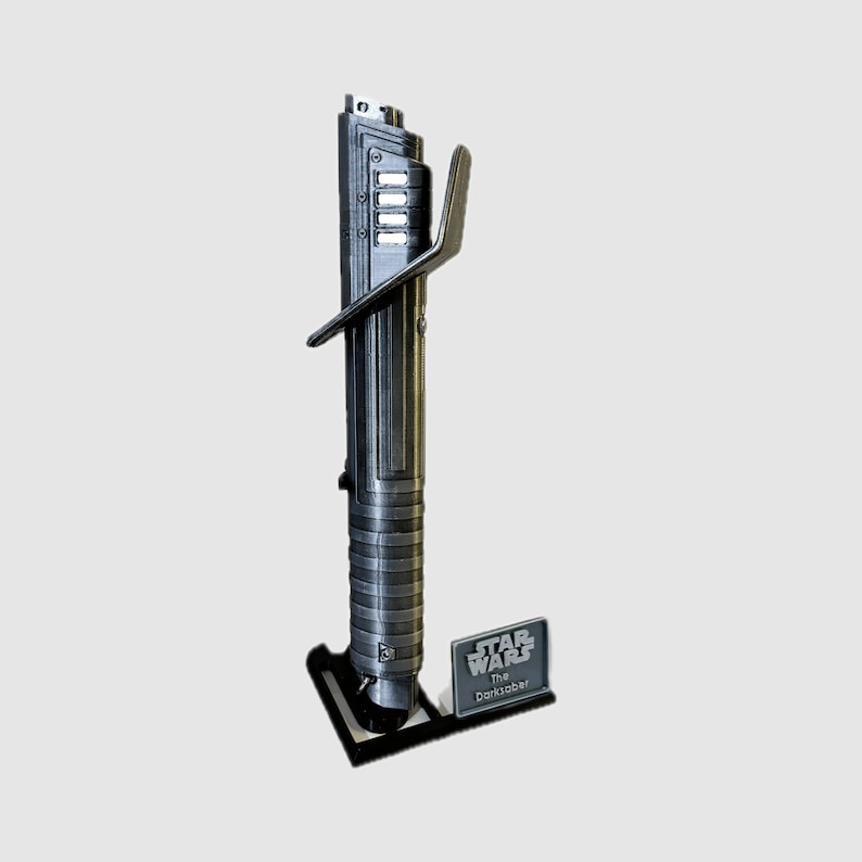 Op de afbeelding: Een zwarte lightsaber-prop met een zilveren handvat en een zwarte standaard. De standaard heeft een klein plakkaat met de tekst "Star Wars The Dark Saber".