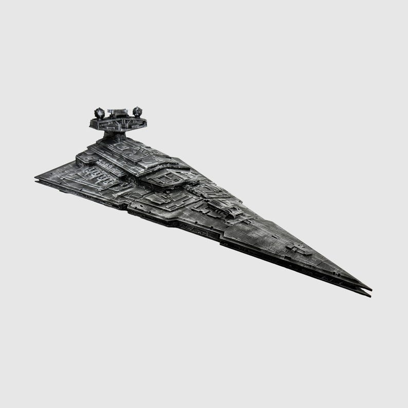 May include: A detailed model of a Star Destroyer spaceship, featuring a gray color scheme with intricate surface detailing. The model has a triangular shape with a long, pointed front and a command tower. The spaceship is a collectible item.
