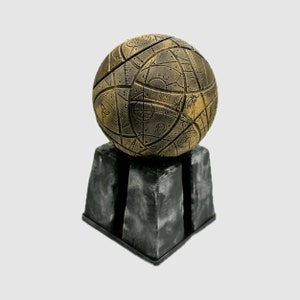 May include: A gold sphere with intricate patterns and markings sits on a black, square base. The sphere appears to be made of metal and has a textured surface.