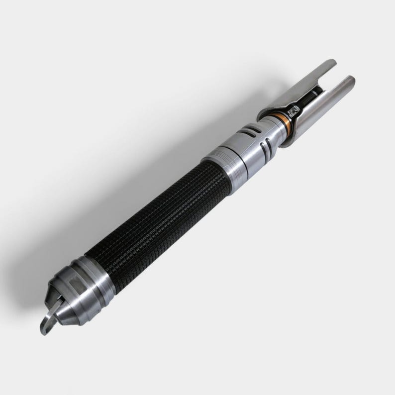 May include: A silver and black lightsaber prop with a textured black grip. The lightsaber has a silver hilt with a detailed design and a blade emitter at the top. The overall design is sleek and futuristic.
