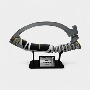 May include: A lightsaber prop from Star Wars: Episode I - The Phantom Menace. The prop is silver, black, and gold, with a curved blade and a handle. The base has a plaque that reads "OPPO RANCISIS - Lightsaber -."