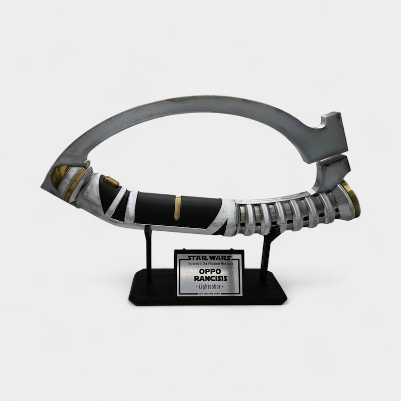 May include: A lightsaber prop from Star Wars: Episode I - The Phantom Menace. The prop is silver, black, and gold, with a curved blade and a handle. The base has a plaque that reads "OPPO RANCISIS - Lightsaber -."