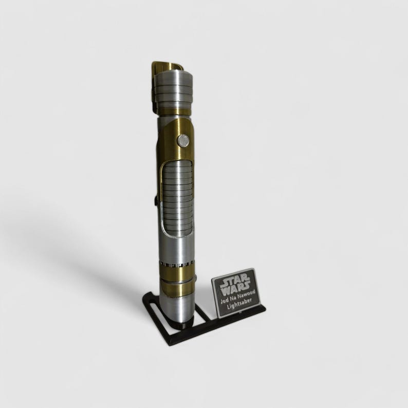 May include: A silver and gold lightsaber with a black stand and a silver plaque that reads "Star Wars Jedi The Newwood Lightsaber".