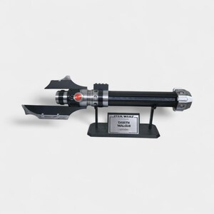 May include: A black and silver Darth Malgus lightsaber replica, with a red button and two side blades. The lightsaber is displayed on a black stand with a Star Wars nameplate.
