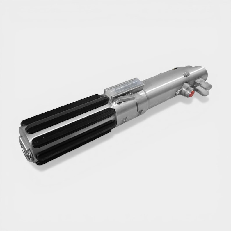 May include: A silver lightsaber prop with a black ribbed handle and a red button. The prop has a metallic finish and detailed mechanical components, suggesting a sci-fi or fantasy theme.