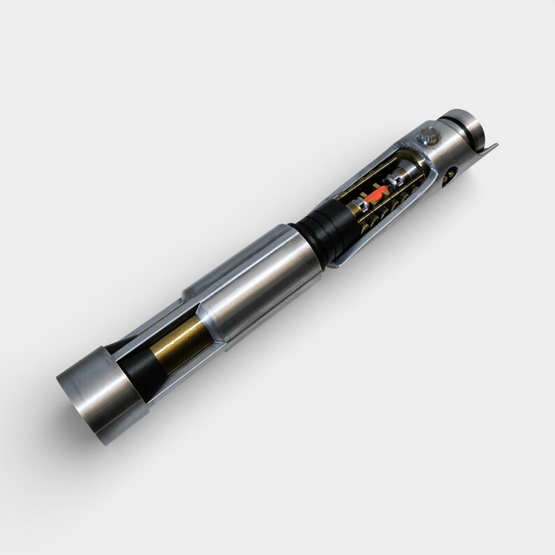 May include: A detailed, cross-section view of a metallic lightsaber prop. The silver hilt reveals internal components, including a red and black core. The design features a cylindrical shape with intricate details, showcasing a blend of mechanical and futuristic elements.