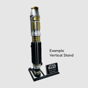 May include: A silver and gold lightsaber with a black handle, displayed on a black stand with a black plaque that reads "STAR WARS Mace Windu Lightsaber". Example Vertical Stand.
