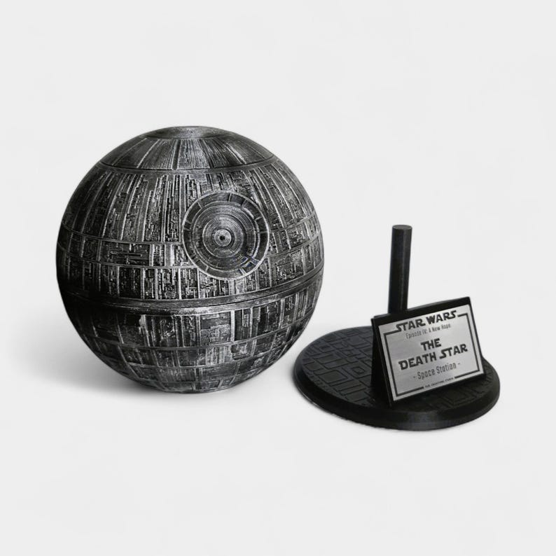 Peut inclure: Maquette sph&eacute;rique d&eacute;taill&eacute;e de l'&Eacute;toile de la Mort de Star Wars, dans des tons de gris et de noir. Le mod&egrave;le est &agrave; c&ocirc;t&eacute; d'un socle noir avec une plaque indiquant "STAR WARS The Death Star - Space Station -."
