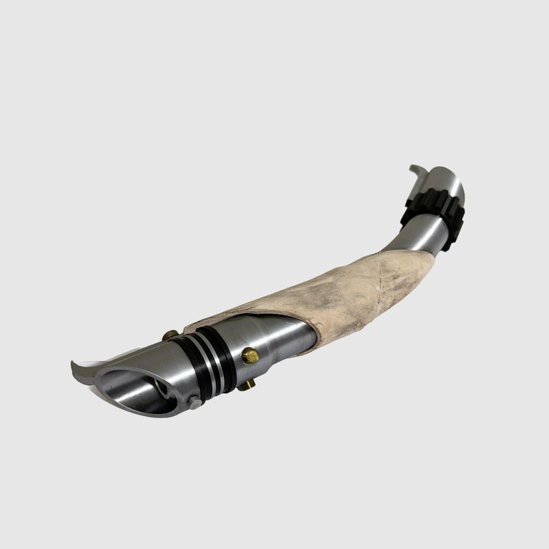 May include: A silver lightsaber with a white, weathered grip. The lightsaber has a black and silver emitter and a black ring around the grip.