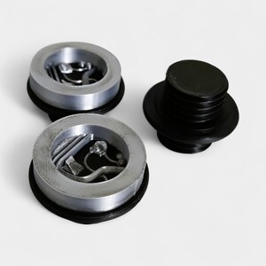 Puede incluir: Tres tapones de botella plateados con bases negras y un tap&oacute;n negro separado. Los tapones plateados tienen un dise&ntilde;o circular con un relieve interior. El tap&oacute;n negro tiene una forma cil&iacute;ndrica con un cuerpo estriado.