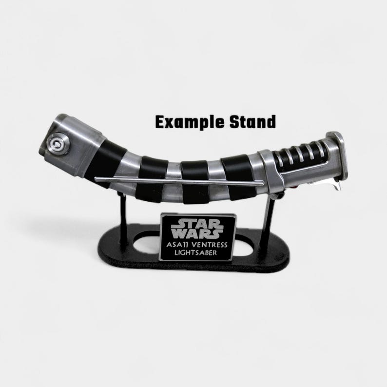 May include: A Star Wars Asajj Ventress lightsaber replica, displayed on a black stand. The lightsaber features silver and black details. The stand has the Star Wars logo and the lightsaber's name. The text "Example Stand" is above the lightsaber.