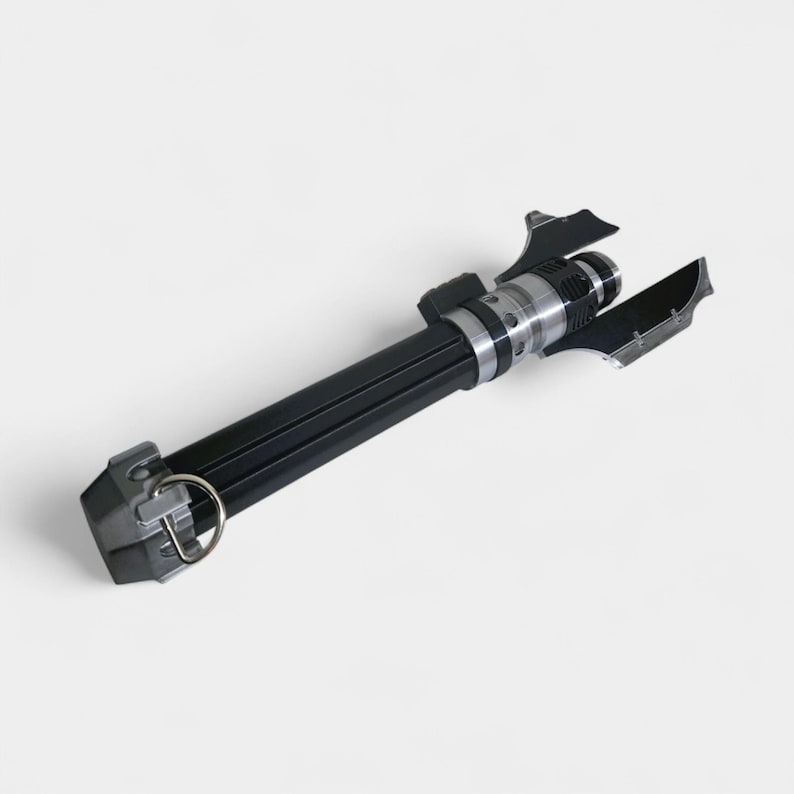 May include: A black and silver lightsaber prop with a cylindrical handle and detailed metallic accents. The prop features a ring at the base and two angled blades near the top. The design is sleek and futuristic, suitable for cosplay or display.