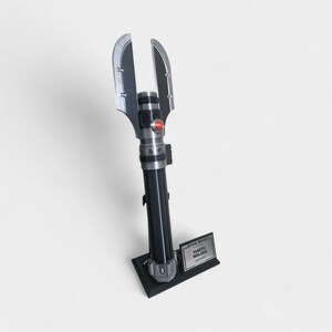 May include: A black and silver Darth Malgus lightsaber replica, standing on a black base. The lightsaber features a red button and a unique blade design. The base includes a nameplate with the Star Wars logo.