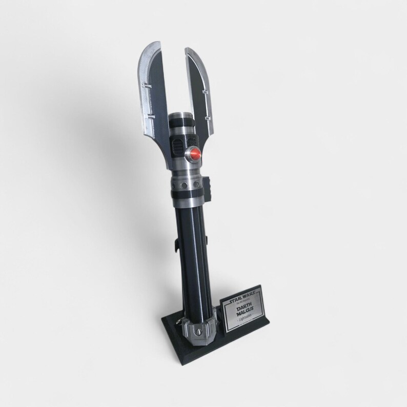 May include: A black and silver Darth Malgus lightsaber replica, standing on a black base. The lightsaber features a red button and a unique blade design. The base includes a nameplate with the Star Wars logo.