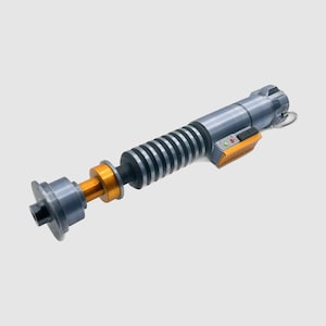 May include: A silver and gold lightsaber prop with a black and silver handle and a gold ring. The lightsaber has a black and silver blade with a silver tip.
