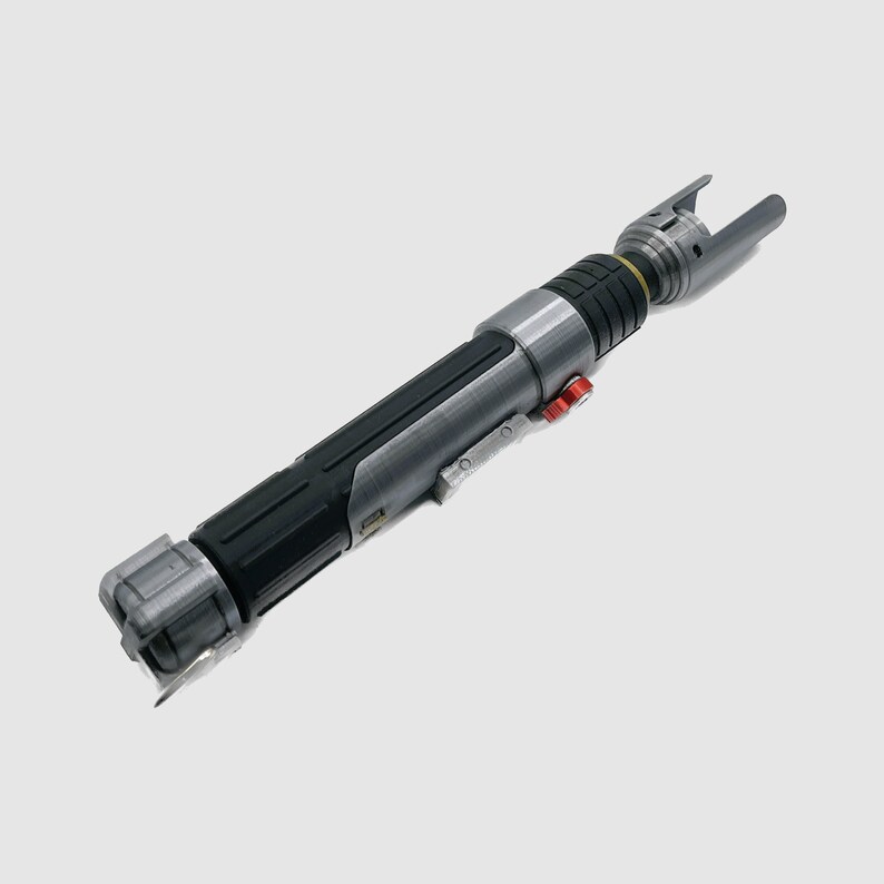 Pode incluir: Um sabre de luz prateado e preto com um bot&atilde;o vermelho e um acento amarelo. O sabre de luz &eacute; um adere&ccedil;o de brinquedo.