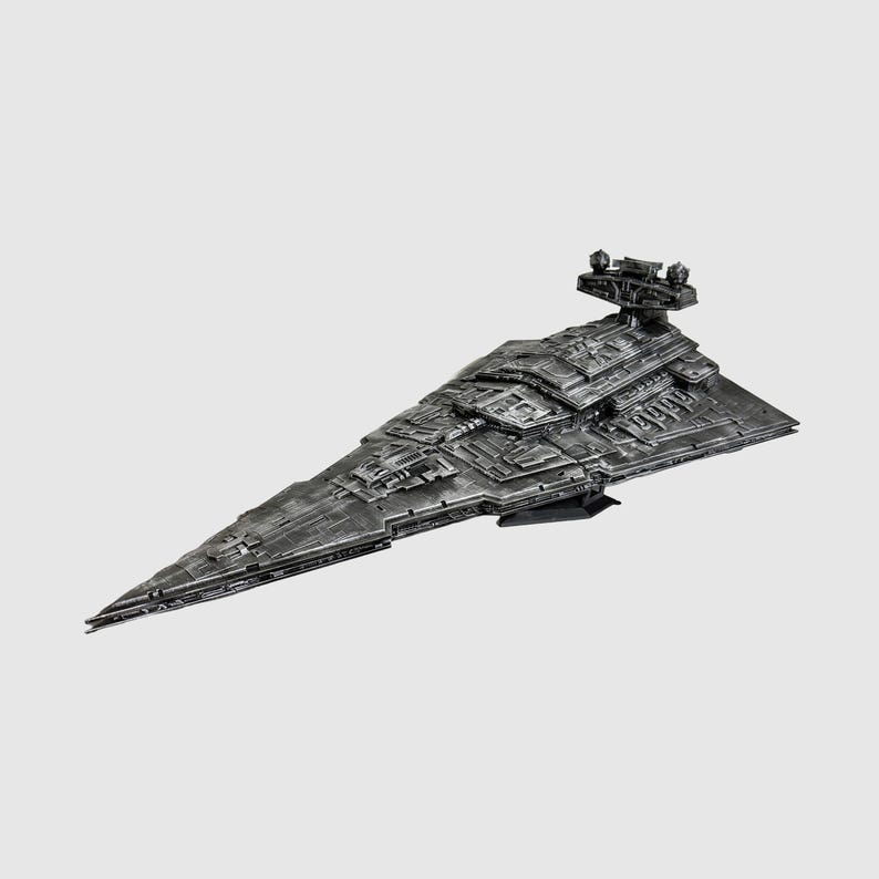 May include: A detailed, metallic gray model of a Star Destroyer spaceship. The model features intricate surface detailing, a prominent bridge structure, and a sharply angled hull. The spaceship is set against a plain white background.