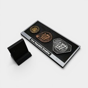 May include: A black rectangular display featuring three New Republic Credits coins in gold, bronze, and silver. The coins have a geometric design. The display also includes a small black stand. The text "New Republic Credits" is visible.